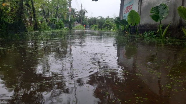 Residents of Mongla navigating through knee-deep water due to severe waterlogging caused by continuous rainfall. Many homes have been inundated, and daily life has come to a halt. (Photo: V7N)