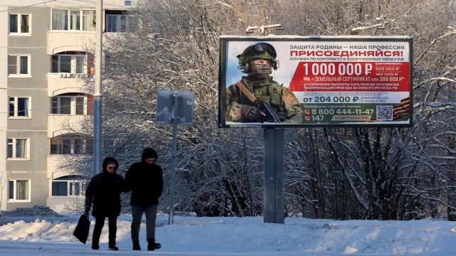 People pass a billboard in the Leningrad Region town of Gatchina that promotes military service under contract in the Russian Armed Forces and includes information about remuneration.