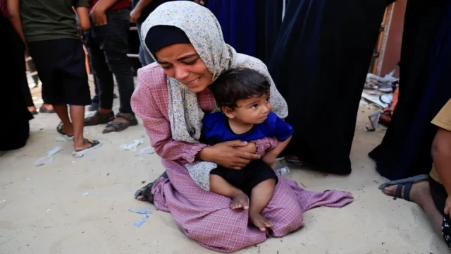 A mourner holds a child while grieving during the funeral of Palestinians killed in an overnight Israeli airstrike on a tent in Khan Younis, according to Gaza's Health Ministry. [Hatem Khaled/Reuters]
