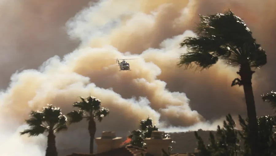 "A helicopter flies over homes in Pacific Palisades as the Palisades Fire threatens the upscale community. The fast-moving brushfire, fueled by strong winds, has caused evacuations and burned over 200 acres in the area."