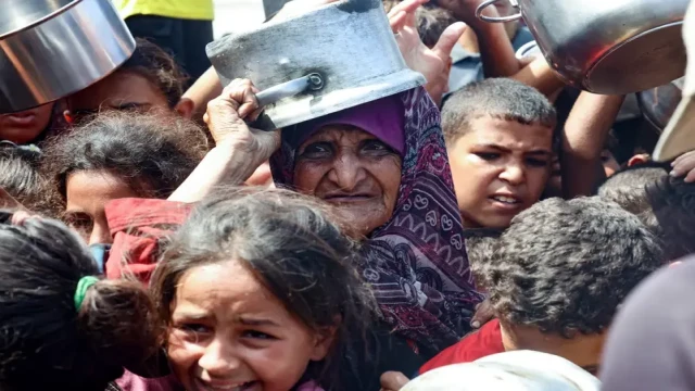 An elderly Palestinian woman and children wait for food at a charity kitchen in Khan Yunis, Gaza, on August 21, 2025. Photo: AFP