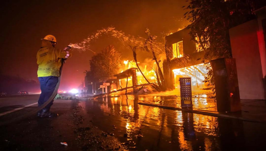 A firefighter battles the Palisades Fire while it burns homes at Pacific Coast Highway amid a powerful windstorm on January 8, 2025 in Los Angeles,.