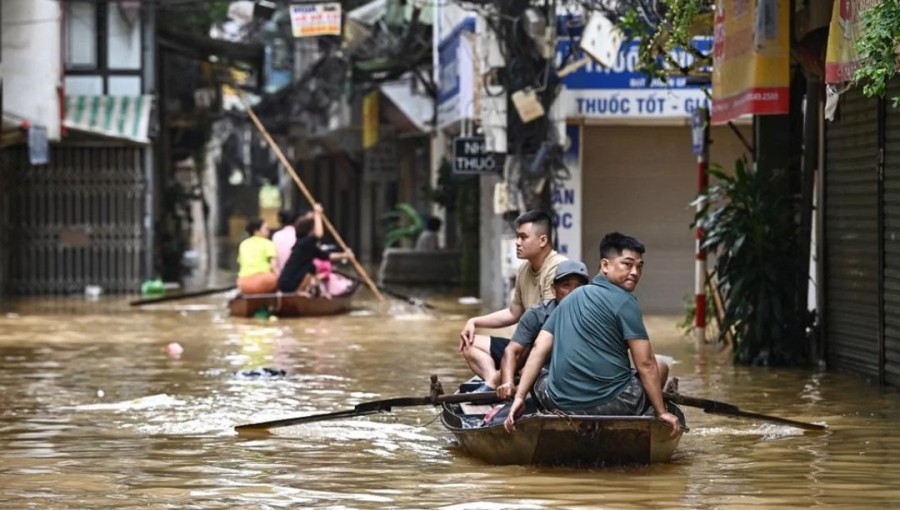 People wade through flood waters on a boat in Hanoi on September 12, 2024, as heavy rains in the aftermath of Typhoon Yagi brought flooding to northern Vietnam.