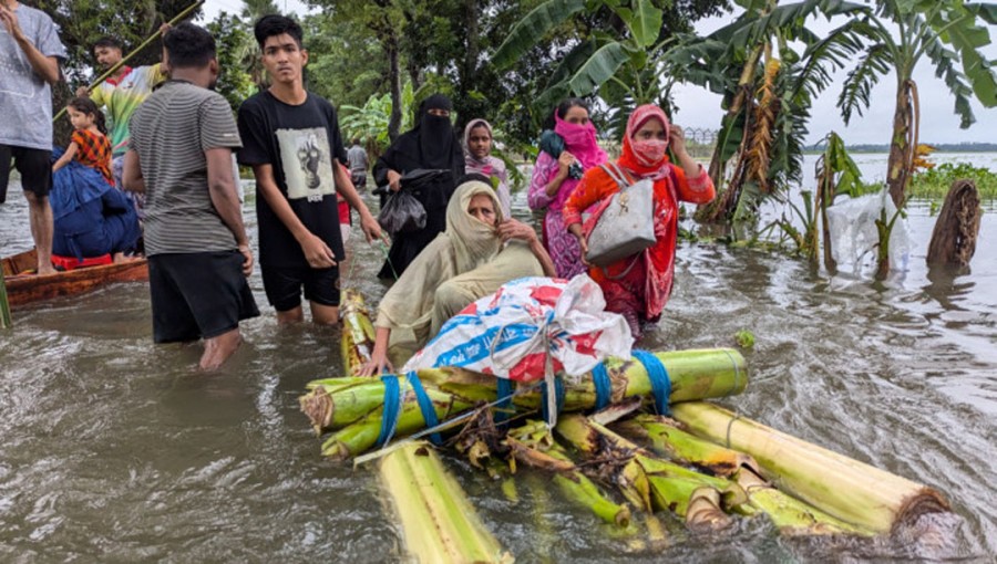 A person tows a raft made of banana trees with an elderly woman on board as local people wade through knee-deep water while others use a boat to move to safer places to escape rushing flood waters at Abupur under Feni sadar upazila on Thursday. Flood waters submerged several other districts including Noakhali, Lakshmipur, Cumilla, Moulvibazar, Sylhet and Khagrachari.