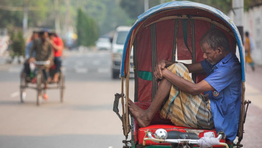 A rickshaw puller takes a break from the scorching heatwave, resting on his rickshaw.