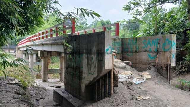 A concrete bridge stands unused over the Louhajang River in Laujana village, Tangail Sadar, with no connecting roads on either side — leaving locals from 30 nearby villages to struggle daily despite nearly Tk 90 lakh spent on construction.