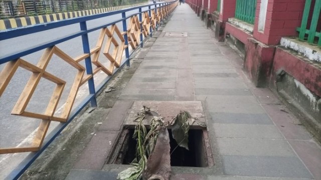 Pedestrians navigate a hazardous stretch of footpath near Rajshahi College Hindu Dormitory, where missing drain covers pose serious safety risks, especially for children and elderly walkers.