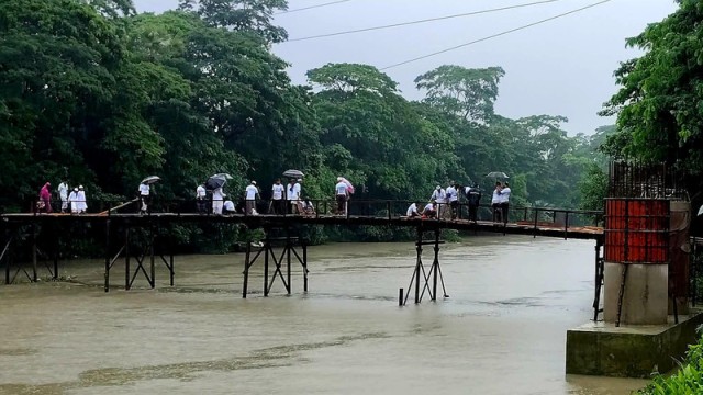 A partially constructed bridge over the Amua Canal in Kathalia, Jhalokathi, remains incomplete for over three years, forcing locals to rely on a risky wooden structure for access to essential services, including the Upazila Health Complex.