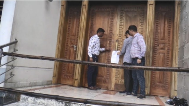 Anti-Corruption Commission officials post a notice on the door of former minister Shajahan Khan’s residence in Madaripur, seeking asset details from his daughter Aishi Khan. (Photo: V7N)
