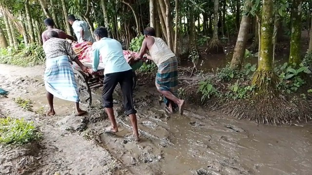 Residents of Salki Matikata in Atpara Upazila, Netrakona, transport a sick patient by van rickshaw along a muddy, broken village road nearly impassable due to monsoon rains, on July 19, 2025.