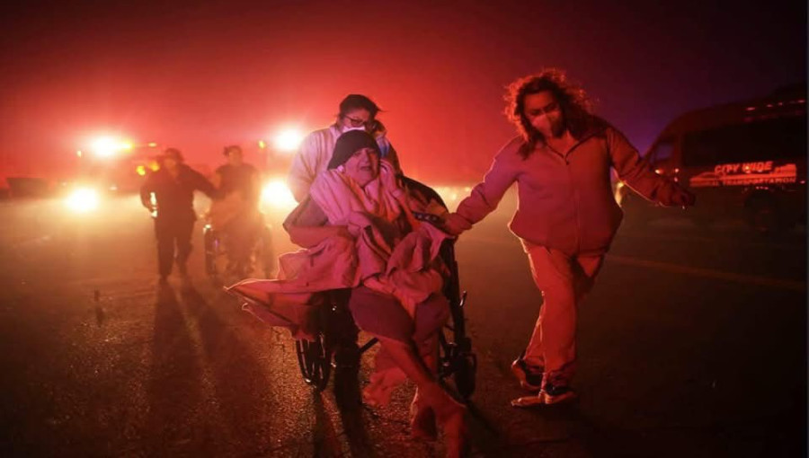 "A person uses a garden hose to protect a neighboring home during the Eaton Fire on Jan. 8, 2025, in Altadena, CA. The wildfires, fueled by intense Santa Ana winds, have destroyed over 1,000 structures and claimed two lives across L.A. County."