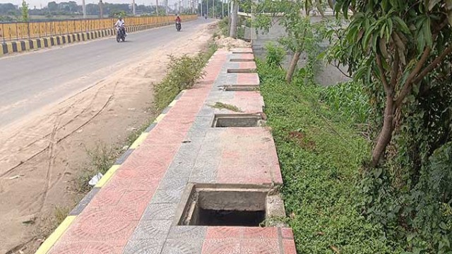 A footpath in Rajshahi where stolen iron drain covers have left open manholes, turning newly renovated city roads into hazardous zones for pedestrians.
